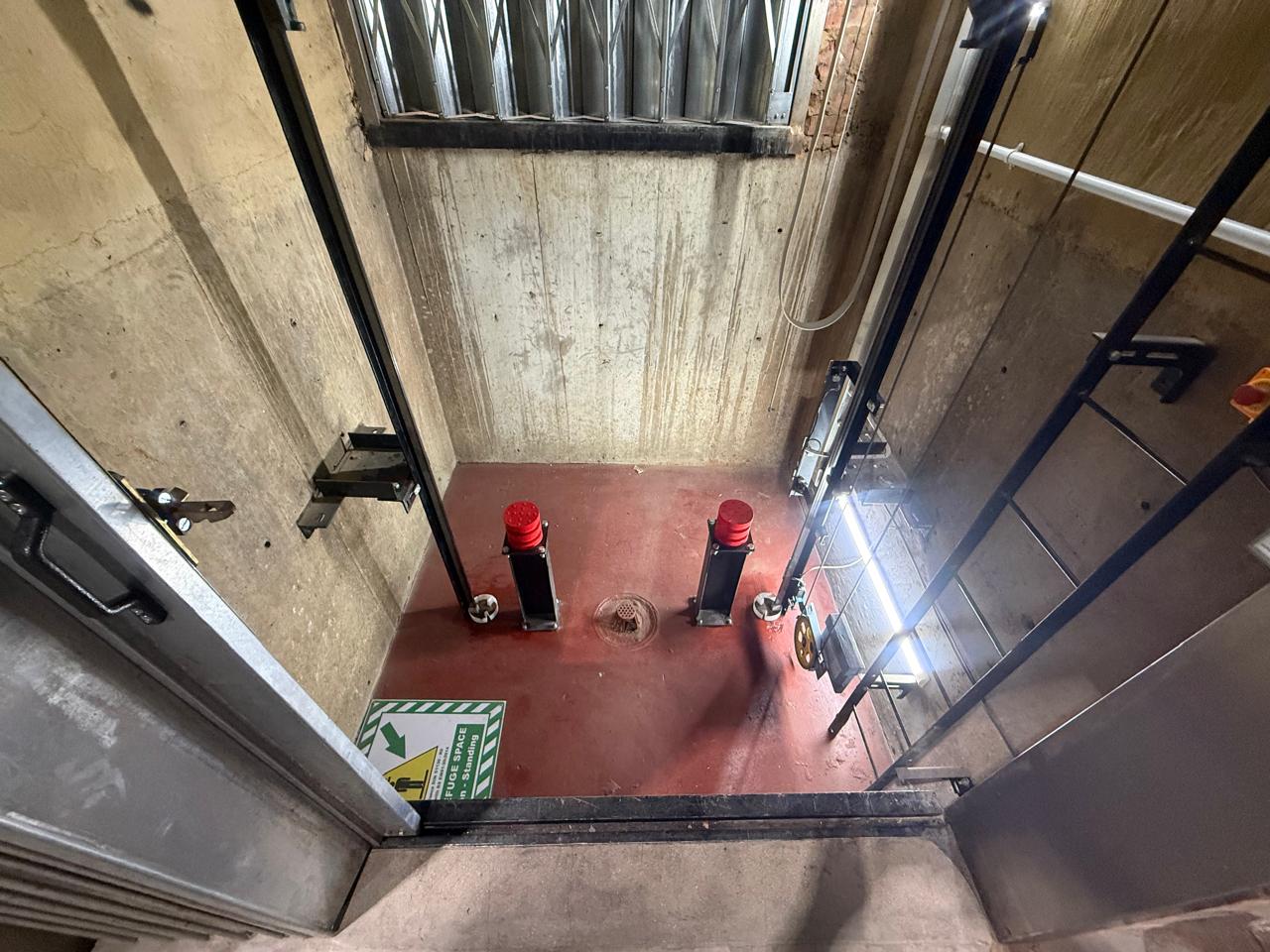 Goods hoist pit with two red buffers on stands, a sealed and painted red pit floor, drain, governor tension sheave and a green safe refuge space decal.