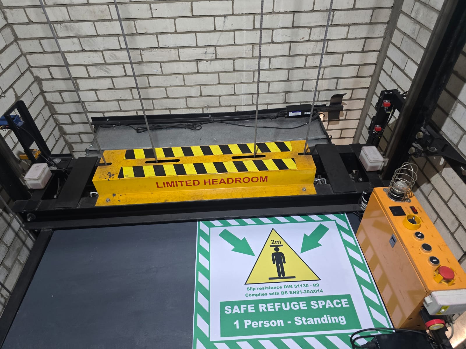 Car top with a yellow limited-headroom barrier, green safe refuge space decal for one standing person, and an orange inspection control station.