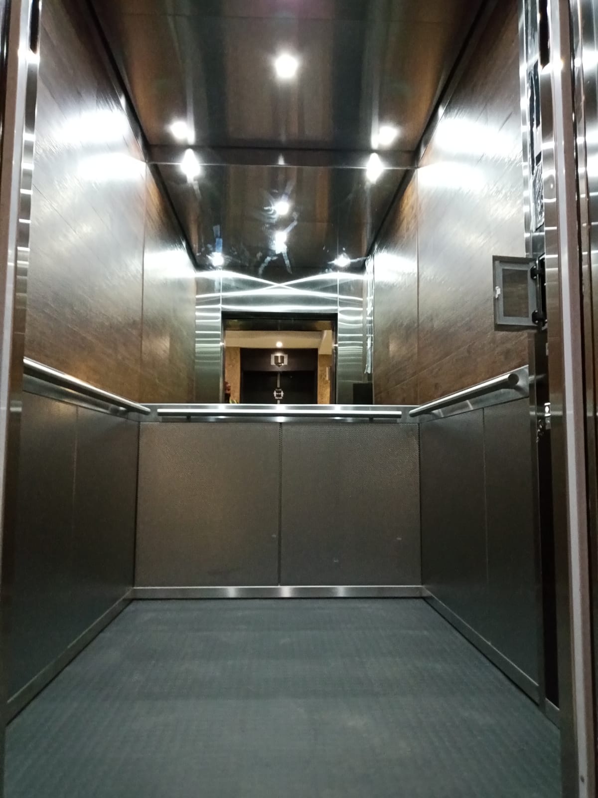 Lift cab finished in bronze-toned stainless steel with textured lower panels, mirrored upper walls and ceiling, and stainless handrails.