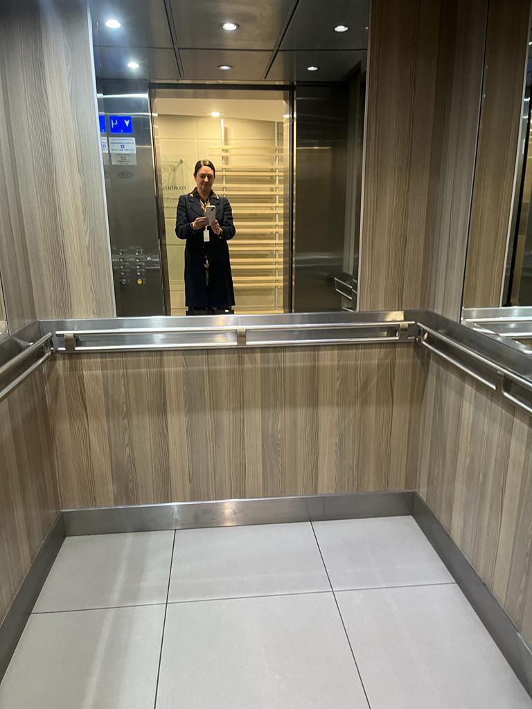 Office lift cab with ash timber-look panels, mirror above the handrail, twin stainless handrails and large format floor tiles.