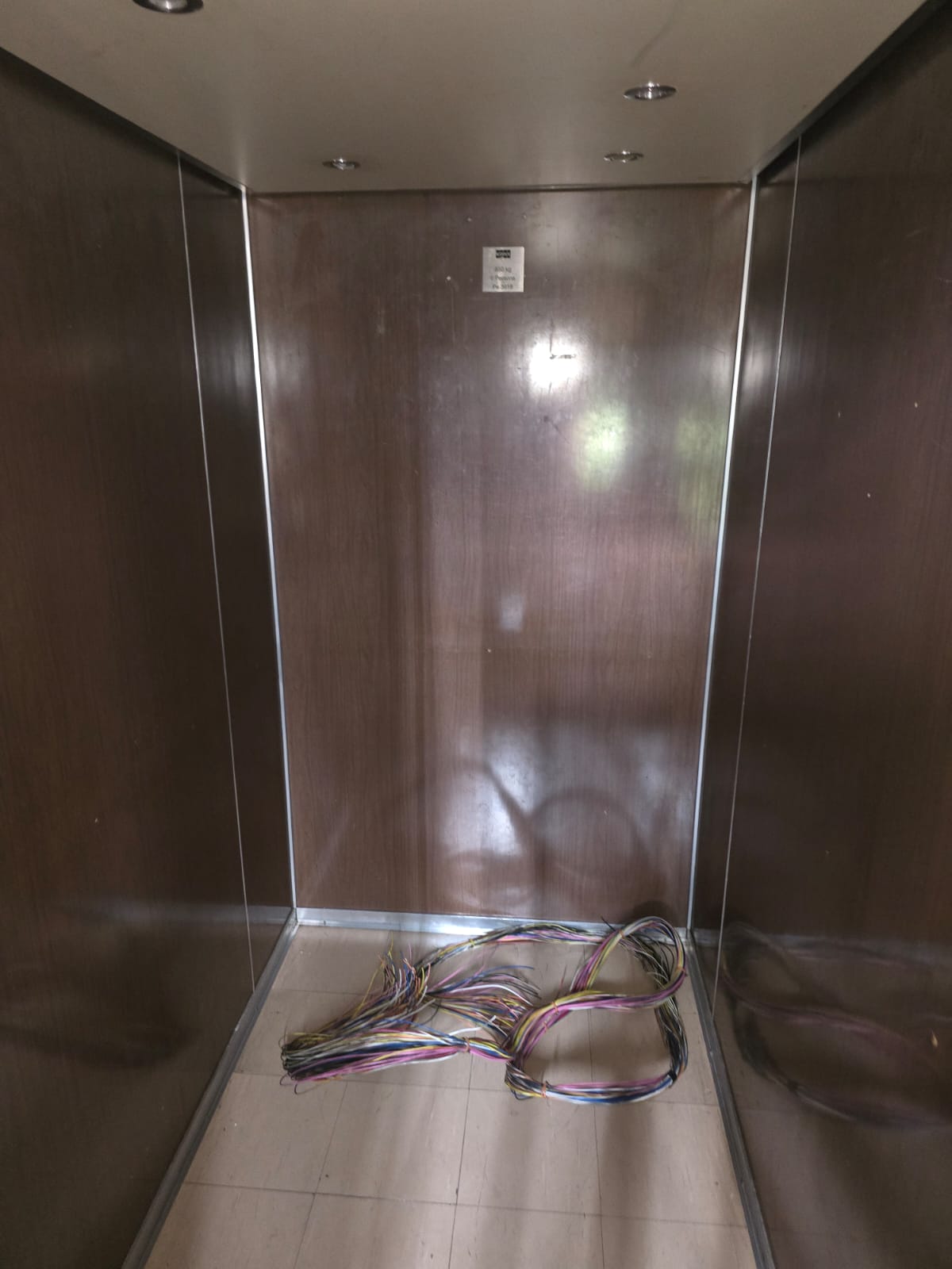 Lift cab mid-refurbishment with wall panels fitted and a loom of travelling cable wiring coiled on the floor awaiting termination.