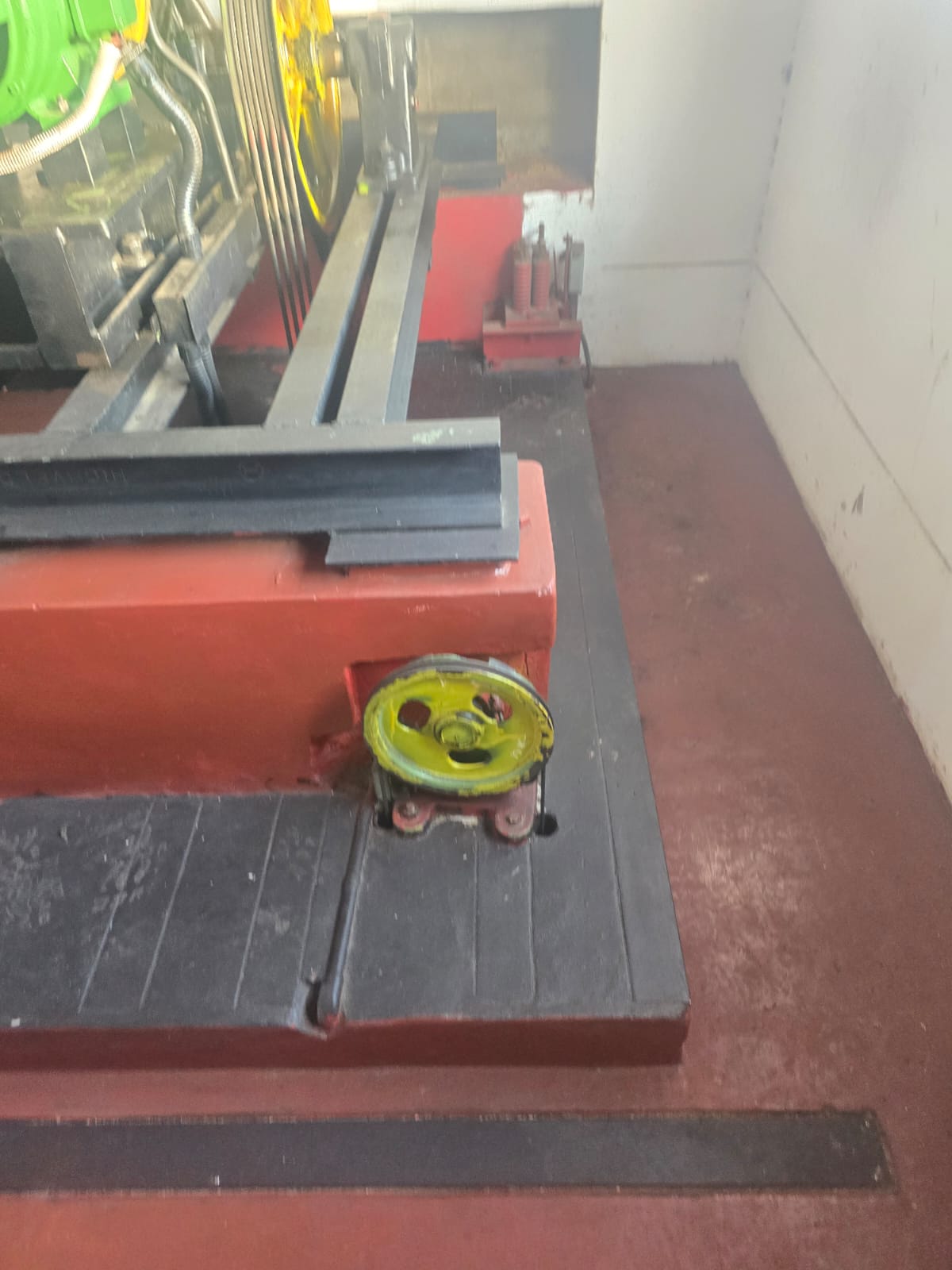Machine room floor with a yellow diverter sheave set into a red plinth and an overspeed governor on its stand against the wall.