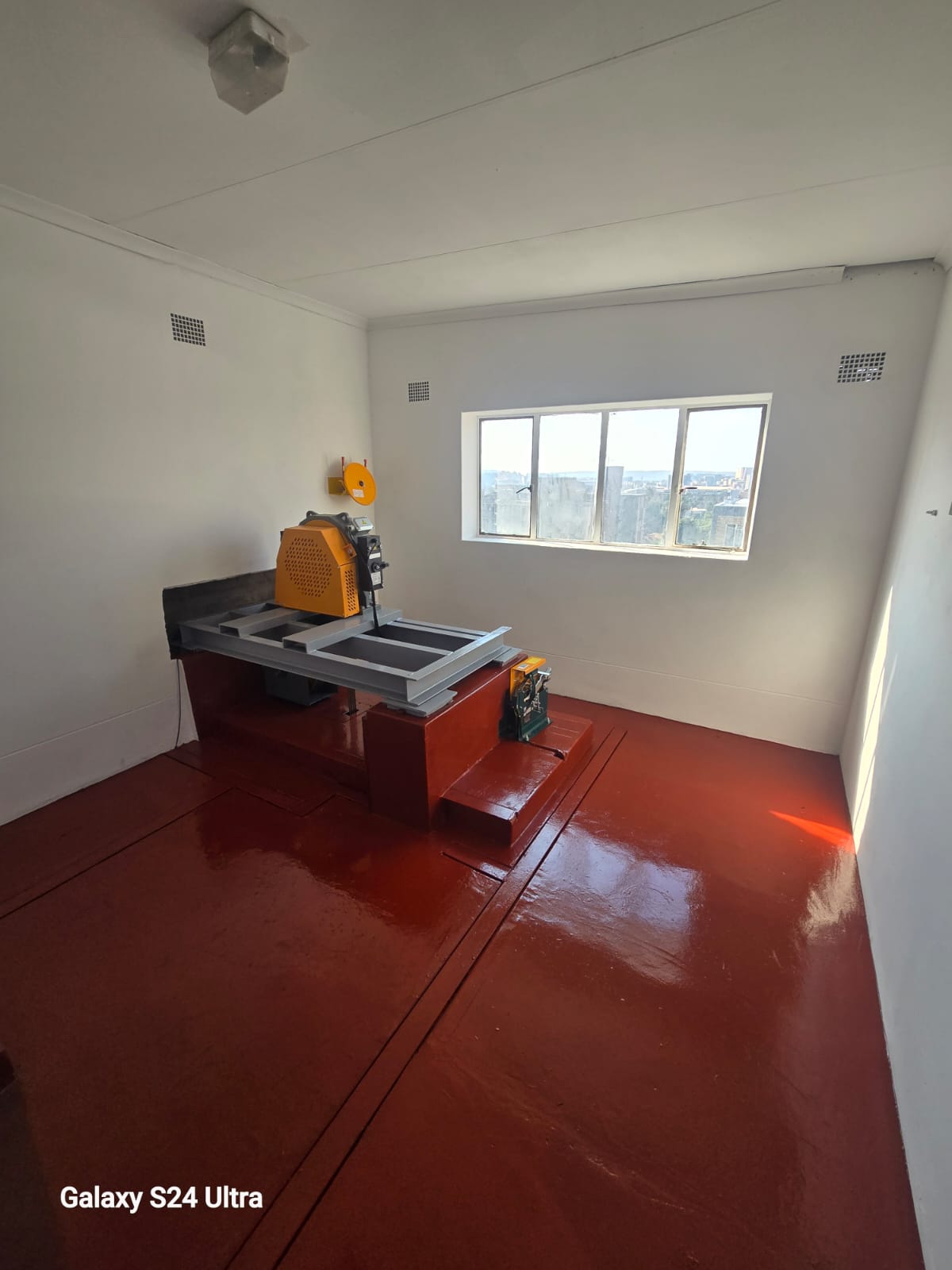 Machine room with a compact drive unit on a grey bedplate over a red plinth, small controller, repainted white walls and a freshly sealed red floor.