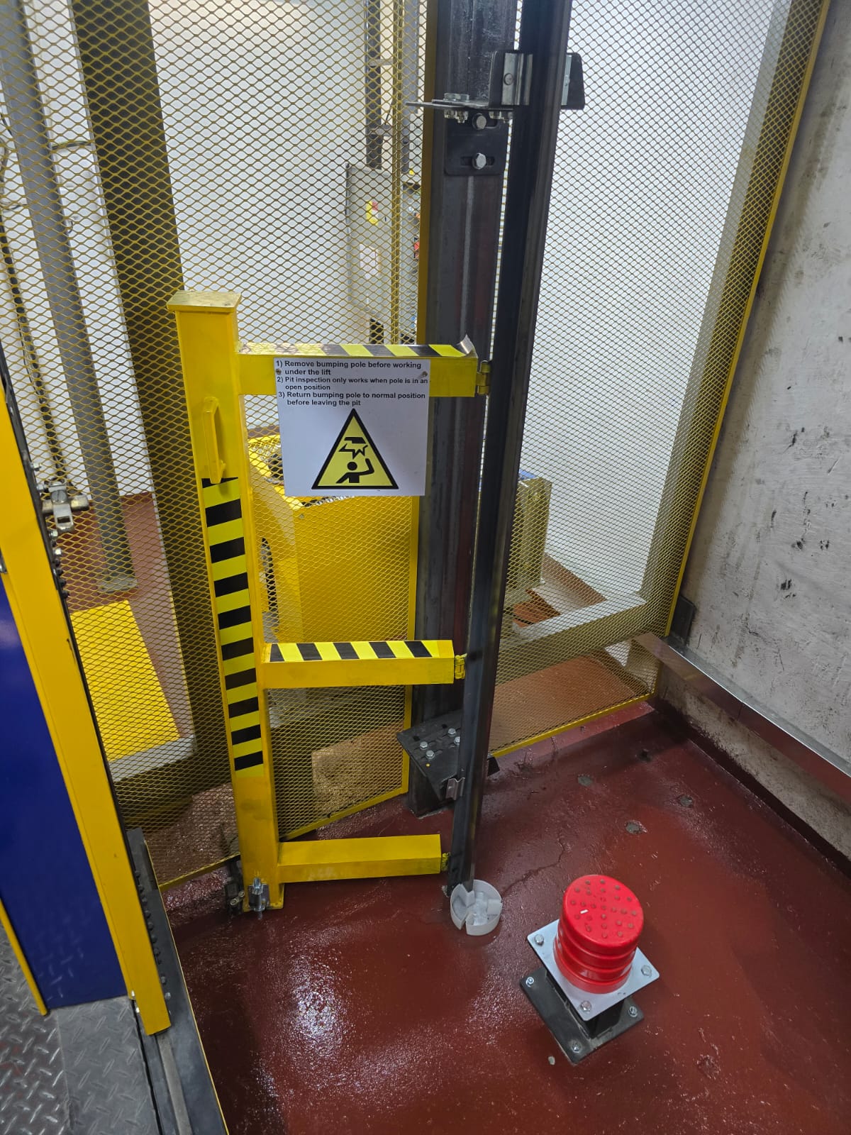 Lift pit with a yellow bumping pole and folding pit ladder, instruction signage, red buffer and a sealed pit floor.