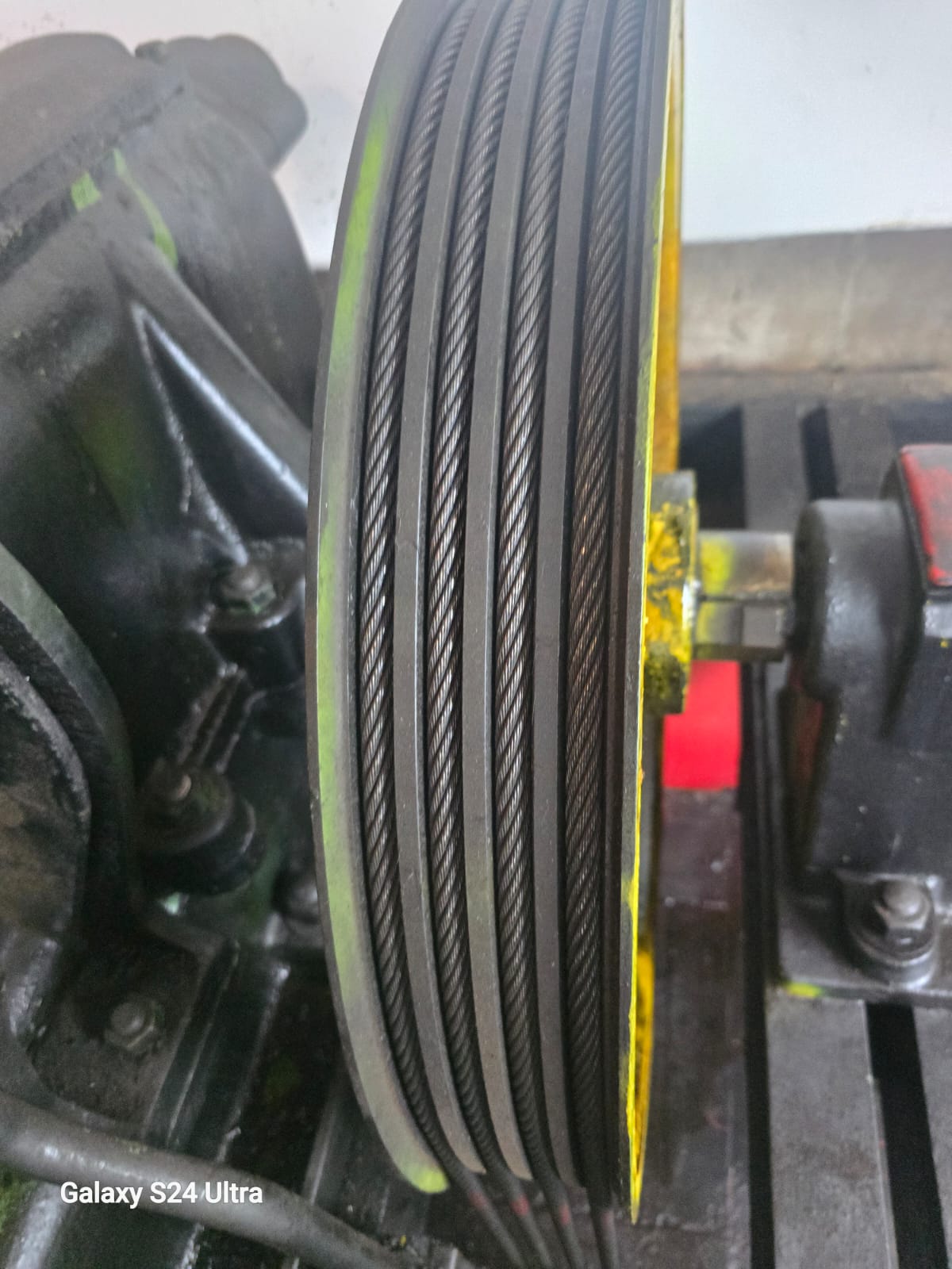 Close-up of a traction sheave with five hoisting ropes seated in the grooves, gearbox and motor behind.